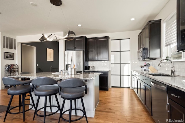 kitchen with sink, stainless steel appliances, a kitchen breakfast bar, backsplash, and a kitchen island