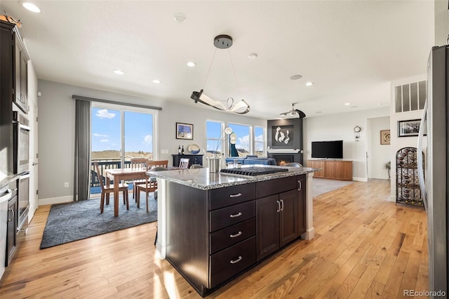 kitchen with dark brown cabinetry, light stone countertops, a center island, decorative light fixtures, and appliances with stainless steel finishes