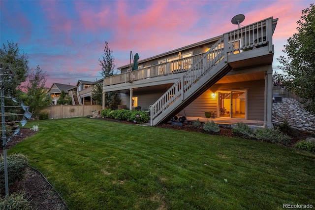 back house at dusk featuring a lawn and a wooden deck