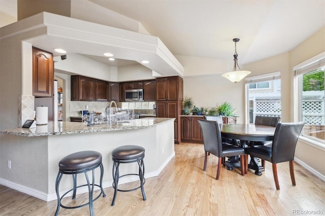3305 White Oak Ln, Highlands Ranch, CO 80129 - kitchen with stainless steel microwave, light wood-style flooring, light stone counters, backsplash, and pendant lighting