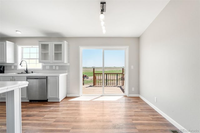 kitchen with stainless steel dishwasher, a sink, light countertops, baseboards, and light wood-style floors