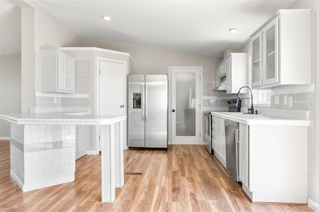 kitchen featuring stainless steel appliances, lofted ceiling, light wood-type flooring, a sink, and glass insert cabinets
