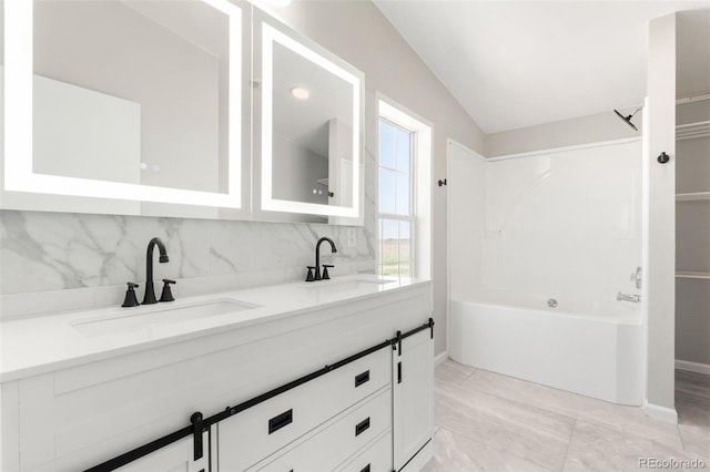 bathroom with decorative backsplash, vaulted ceiling, double vanity, and baseboards