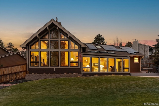 back house at dusk featuring a yard and solar panels