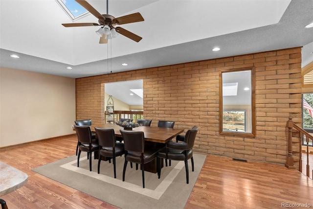 dining room with brick wall, vaulted ceiling with skylight, ceiling fan, and light hardwood / wood-style flooring