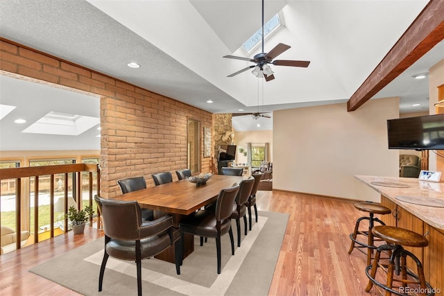 dining area with brick wall, vaulted ceiling with skylight, ceiling fan, and light hardwood / wood-style floors