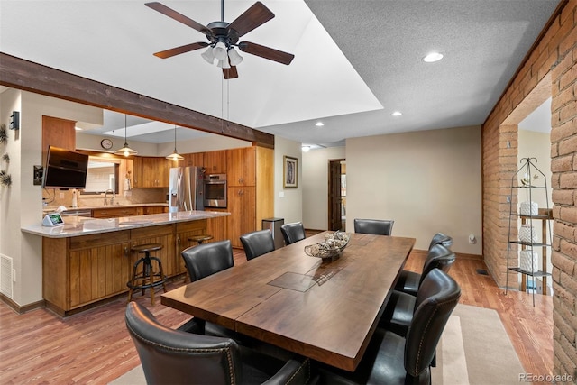 dining room featuring sink, beam ceiling, a textured ceiling, and light wood-type flooring