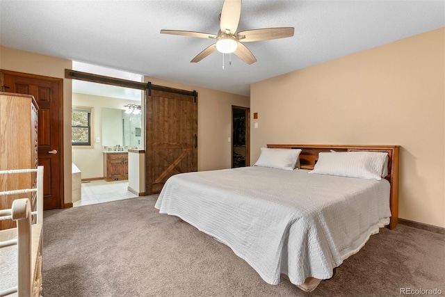 bedroom with light colored carpet, a barn door, ceiling fan, and ensuite bathroom