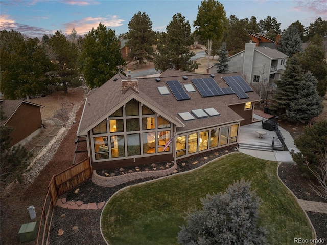 back house at dusk with a yard and solar panels