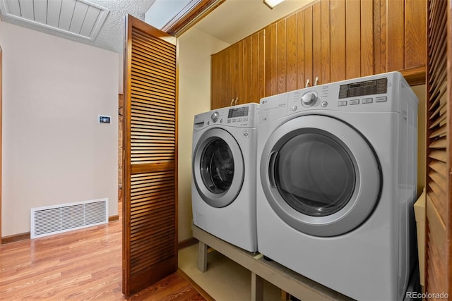 clothes washing area featuring cabinets, washer and clothes dryer, light wood-type flooring, and a textured ceiling