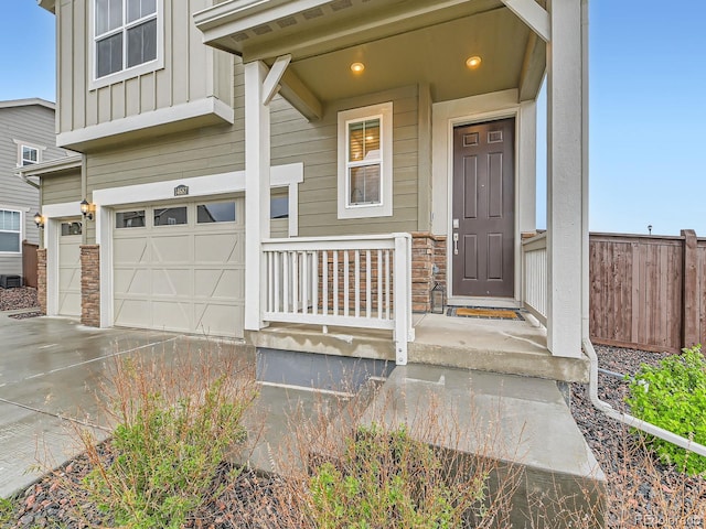 doorway to property featuring board and batten siding, a garage, concrete driveway, and fence