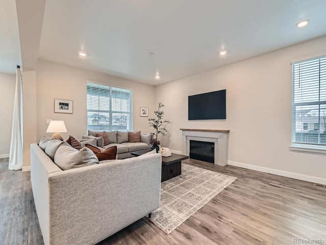 living room featuring wood finished floors, a glass covered fireplace, baseboards, and recessed lighting