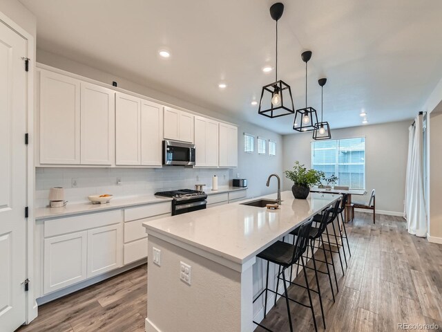 kitchen with appliances with stainless steel finishes, a sink, light wood-style flooring, an island with sink, and recessed lighting