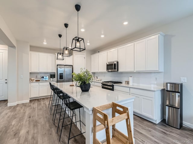 kitchen with appliances with stainless steel finishes, light wood-style flooring, white cabinetry, a breakfast bar area, and recessed lighting