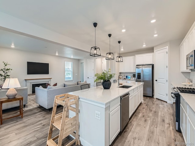 kitchen with stainless steel appliances, a sink, open floor plan, light wood-style flooring, and white cabinets