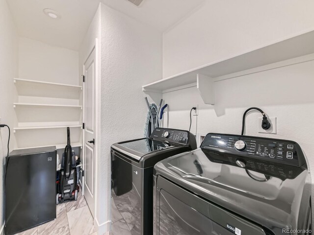 washroom with independent washer and dryer, light marble finish flooring, and a textured wall