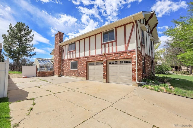 view of front facade featuring a garage, concrete driveway, a chimney, brick siding, and fence