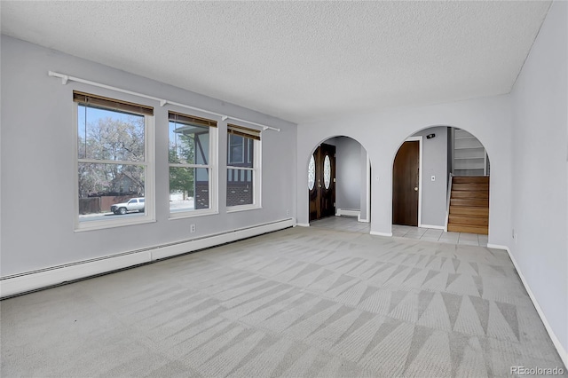 spare room featuring arched walkways, a baseboard radiator, light carpet, a textured ceiling, and stairs