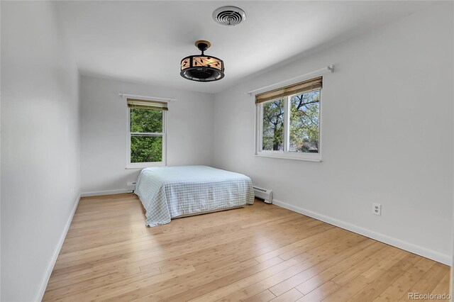 bedroom with baseboards, a baseboard heating unit, and light wood-type flooring