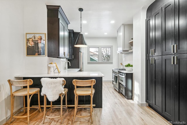 kitchen with a kitchen breakfast bar, decorative light fixtures, light hardwood / wood-style flooring, kitchen peninsula, and high end stove