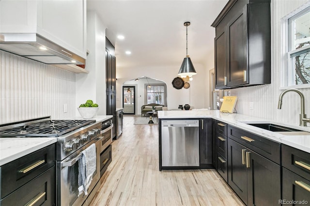 kitchen featuring appliances with stainless steel finishes, custom range hood, sink, decorative light fixtures, and light stone counters