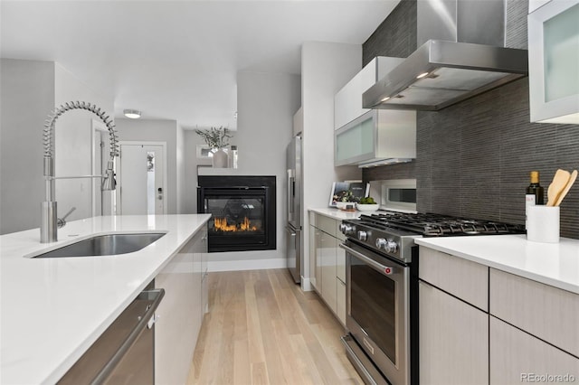 kitchen featuring wall chimney range hood, appliances with stainless steel finishes, light countertops, and a sink