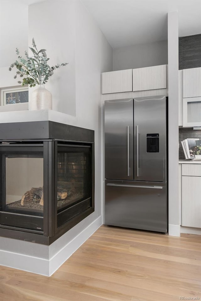 kitchen featuring modern cabinets, a multi sided fireplace, built in refrigerator, and wood finished floors