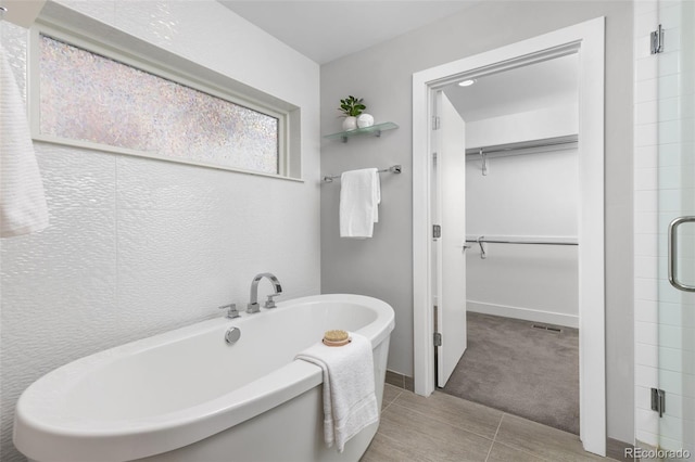 full bathroom with a freestanding tub, a stall shower, a walk in closet, and baseboards