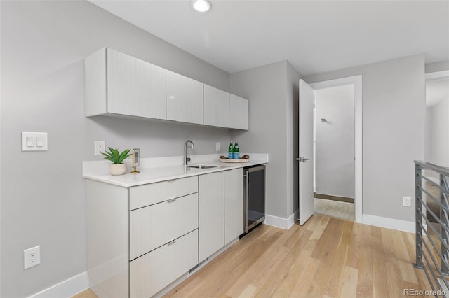 kitchen with wine cooler, light wood finished floors, light countertops, white cabinetry, and a sink