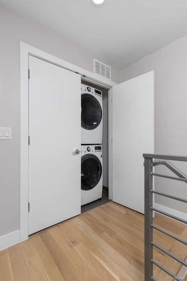 clothes washing area featuring laundry area, visible vents, wood finished floors, and stacked washer and clothes dryer