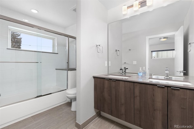 full bathroom with toilet, double vanity, combined bath / shower with glass door, and a sink