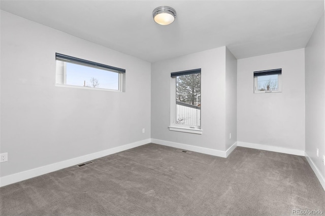 carpeted empty room featuring a healthy amount of sunlight, visible vents, and baseboards