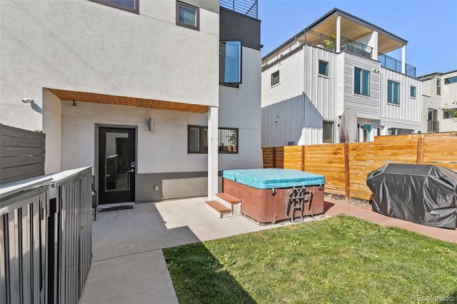 back of property featuring a lawn, stucco siding, fence private yard, and a hot tub