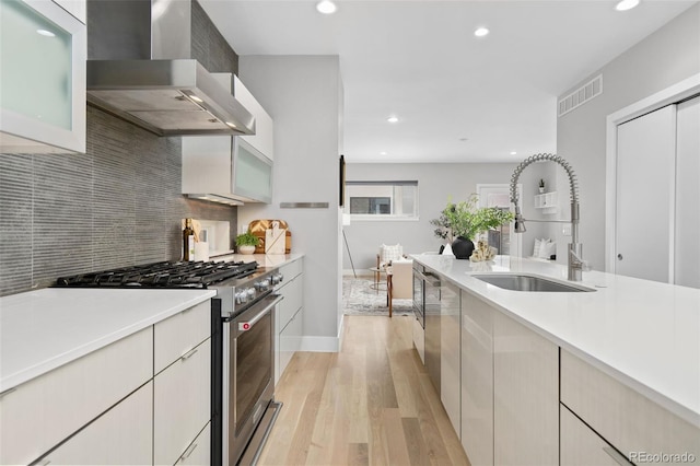 kitchen featuring high end stove, a sink, visible vents, light countertops, and wall chimney range hood