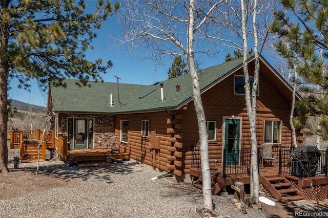 view of front of property featuring a wooden deck, log exterior, and a shingled roof