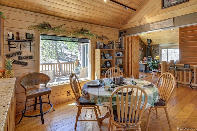 dining room featuring wooden ceiling, light wood-type flooring, a wood stove, and lofted ceiling