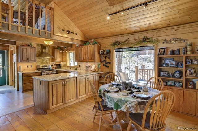 kitchen with light wood finished floors, wall chimney exhaust hood, stainless steel range with gas cooktop, and a sink