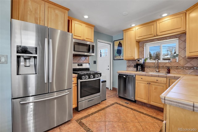 kitchen with stainless steel appliances, sink, light tile patterned floors, light brown cabinets, and tile counters