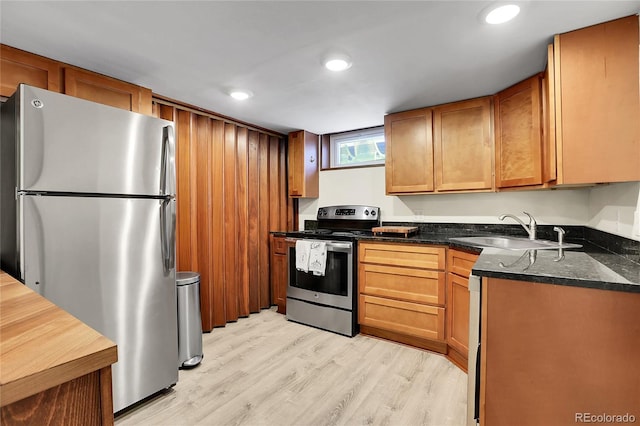 kitchen with dark stone countertops, sink, light hardwood / wood-style flooring, and appliances with stainless steel finishes