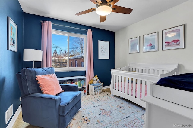 bedroom with a crib, light hardwood / wood-style floors, and ceiling fan