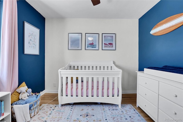 bedroom featuring ceiling fan, light hardwood / wood-style floors, and a nursery area