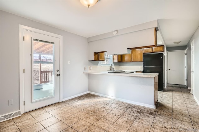 kitchen featuring black refrigerator, plenty of natural light, kitchen peninsula, and light tile patterned flooring