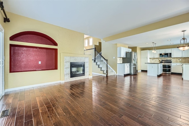 9975 Blackbird Cir, Highlands Ranch, CO 80130 - unfurnished living room with a tiled fireplace, dark wood finished floors, and stairs