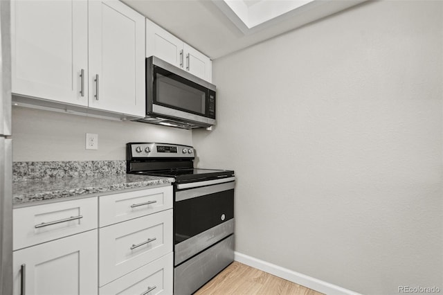 kitchen featuring stainless steel appliances, white cabinetry, light stone countertops, a skylight, and light wood-type flooring