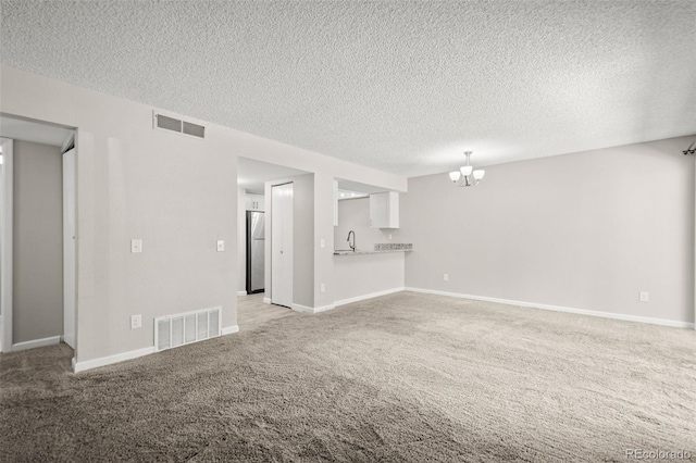 unfurnished living room featuring sink, an inviting chandelier, a textured ceiling, and light carpet