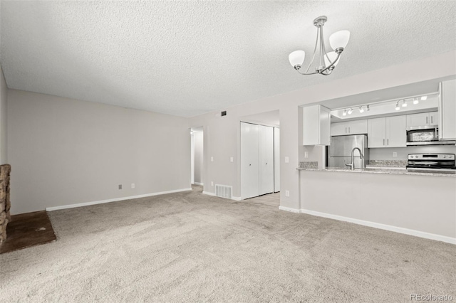 unfurnished living room with a textured ceiling, light carpet, a chandelier, and sink