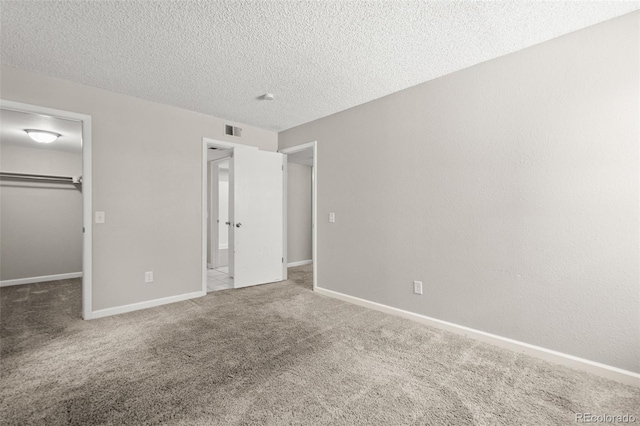 unfurnished bedroom with a textured ceiling, a closet, a walk in closet, and carpet floors