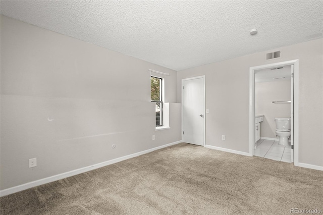 unfurnished bedroom with a textured ceiling, light carpet, and ensuite bathroom