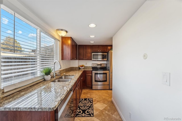 kitchen featuring baseboards, appliances with stainless steel finishes, light stone countertops, a sink, and recessed lighting