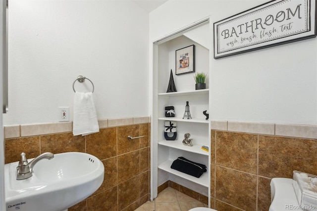 bathroom featuring toilet, tile patterned flooring, tile walls, and a sink